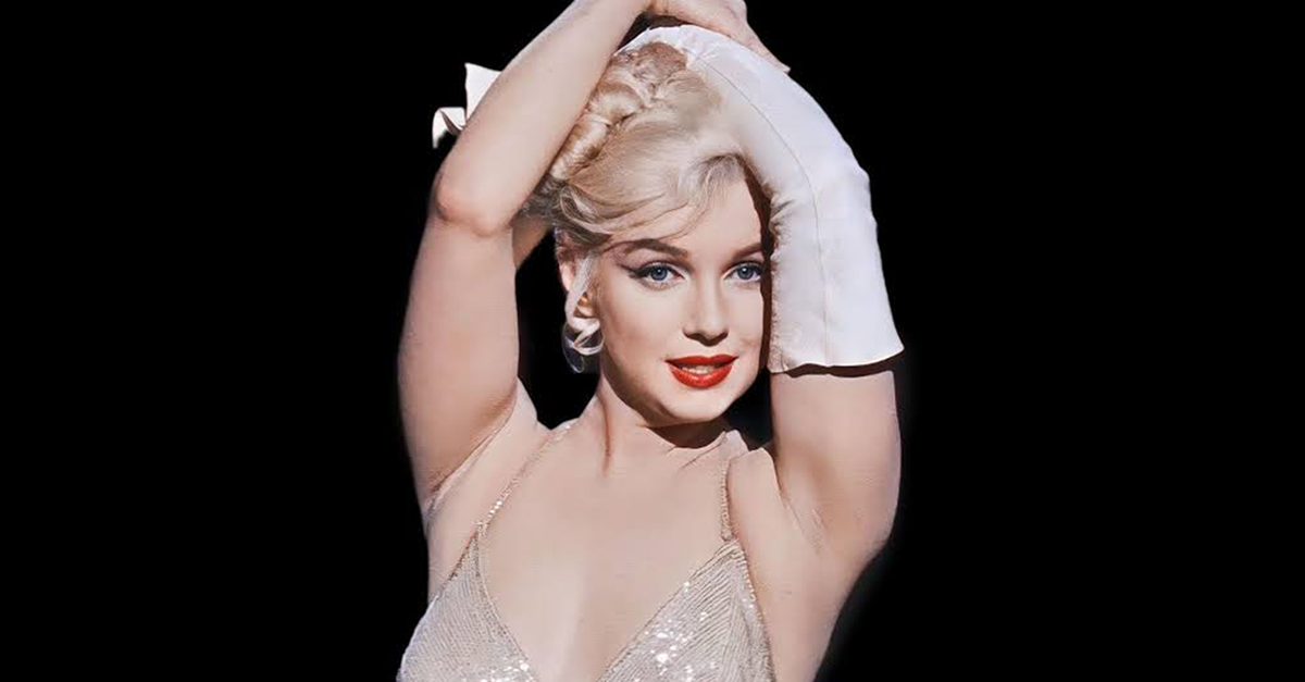Marilyn Monroe with her arms over her head in a dress with one long glove on one arm in the film Let’s Make Love (1960)