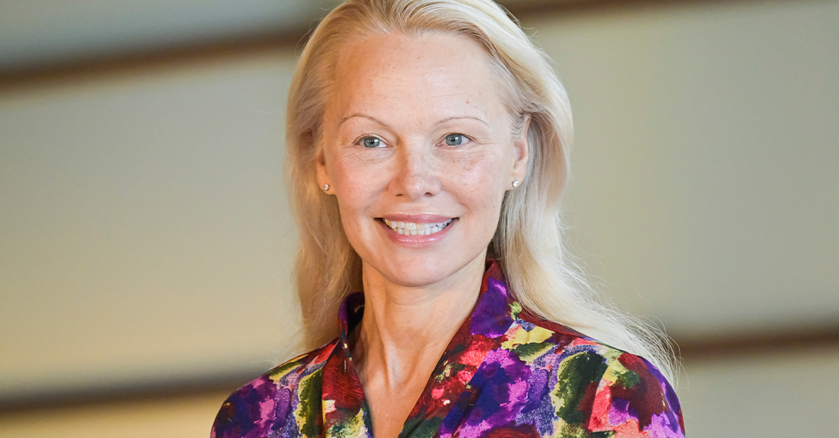 Pamela Anderson at a "The Last Showgirl" photo call, smiling and wearing a floral blouse.