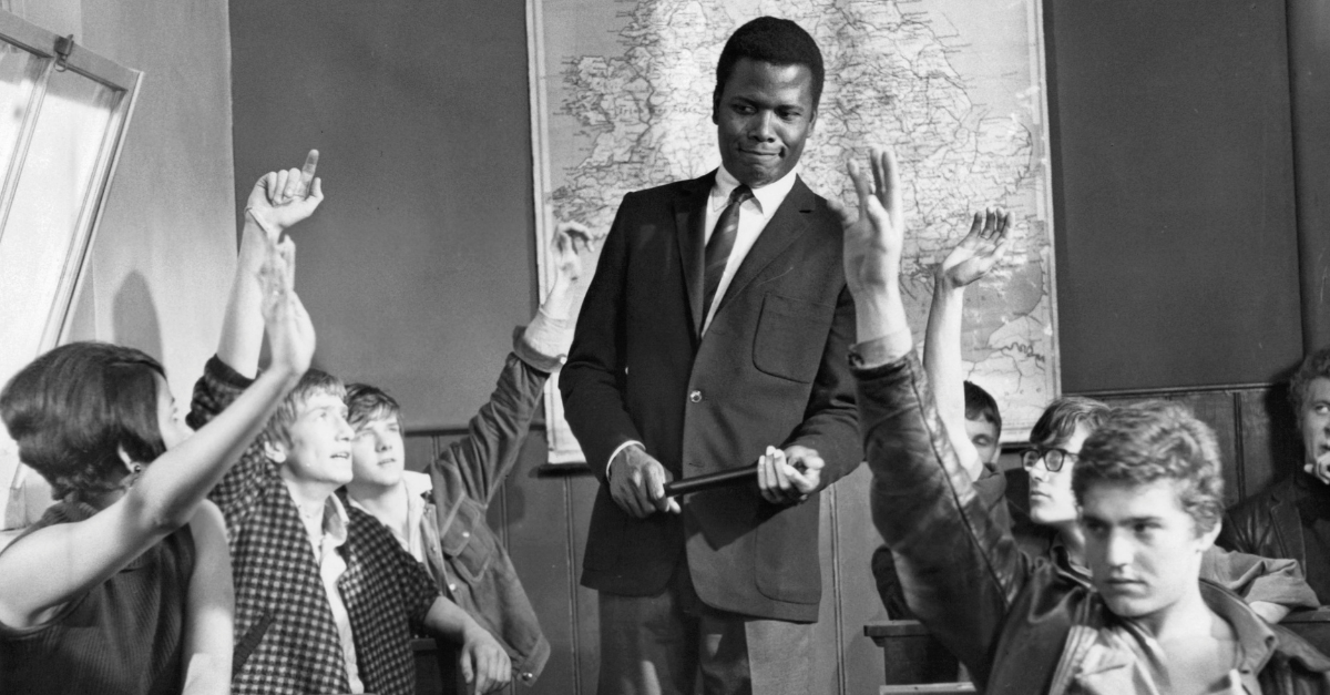 Sidney Poitier standing in classroom as students raise their hands in a scene from the film 'To Sir, With Love', 1967.