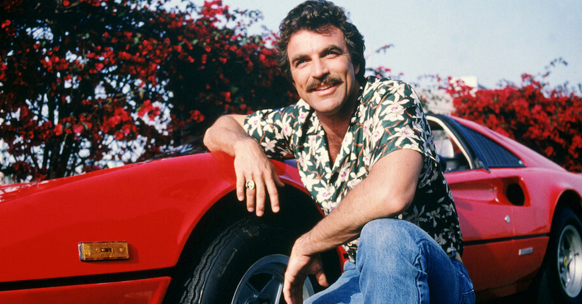 Tom Selleck as the titular investigator in the television series 'Magnum, P.I.', circa 1985. He is posing with his red Ferrari 308