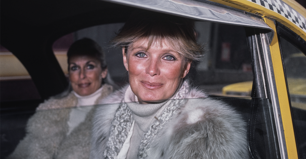 American actress Linda Evans, wearing a grey fur coat, sitting in the backseat of a Checker Cab
